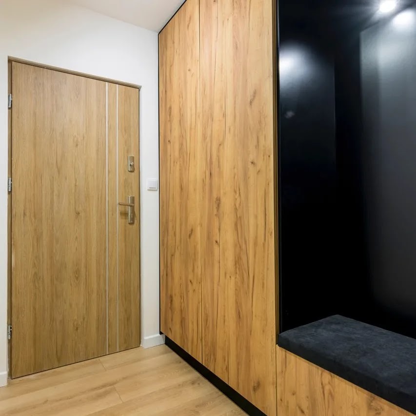 Wnętrze przedpokoju z drewnianą szafą na wymiar z czarnym wnęką na siedzisko i drewnianymi drzwiami z srebrnymi paskami.