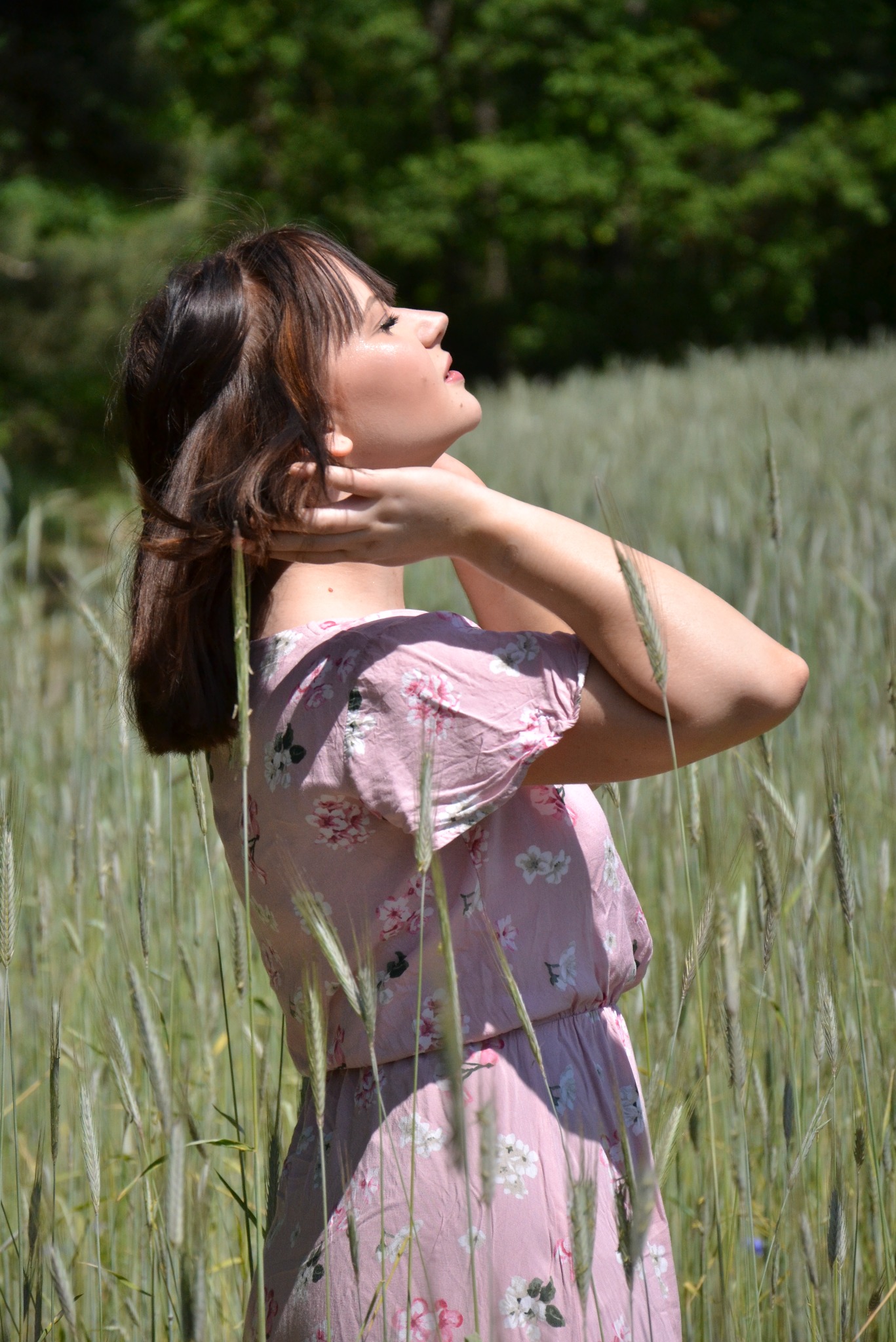 Kobieta w kwiecistej sukience, stojąca na polu zboża z głową zadartą do góry