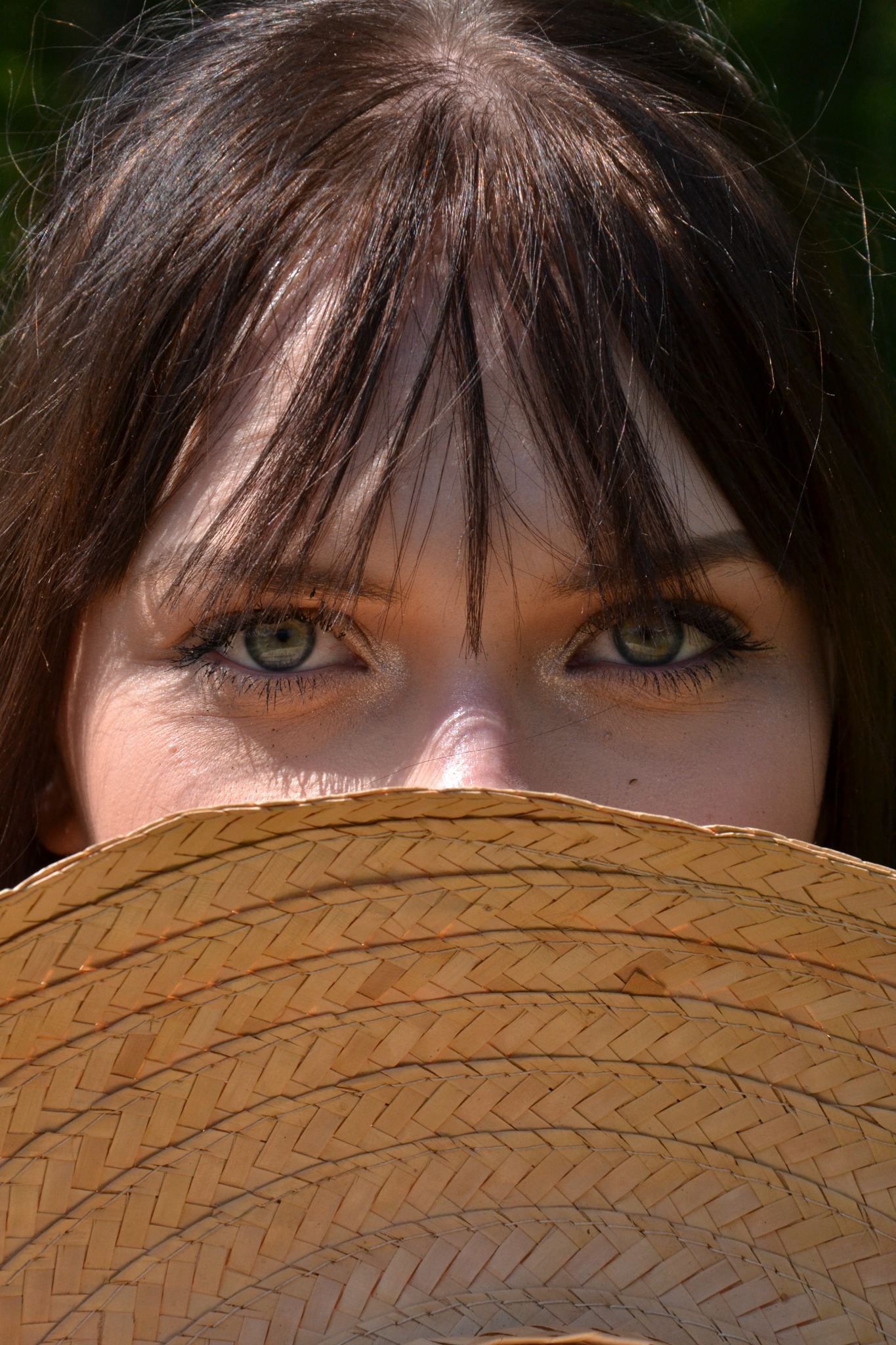 Portret kobiety z zielonymi oczami, częściowo zasłoniętej słomkowym kapeluszem, patrzącej w obiektyw.