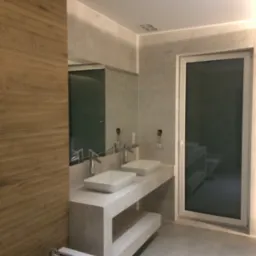 Nowoczesna łazienka z dwoma umywalkami nablatowymi na blacie z szarego kamienia, bidetem z chromowaną armaturą i dużym oknem balkonowym.