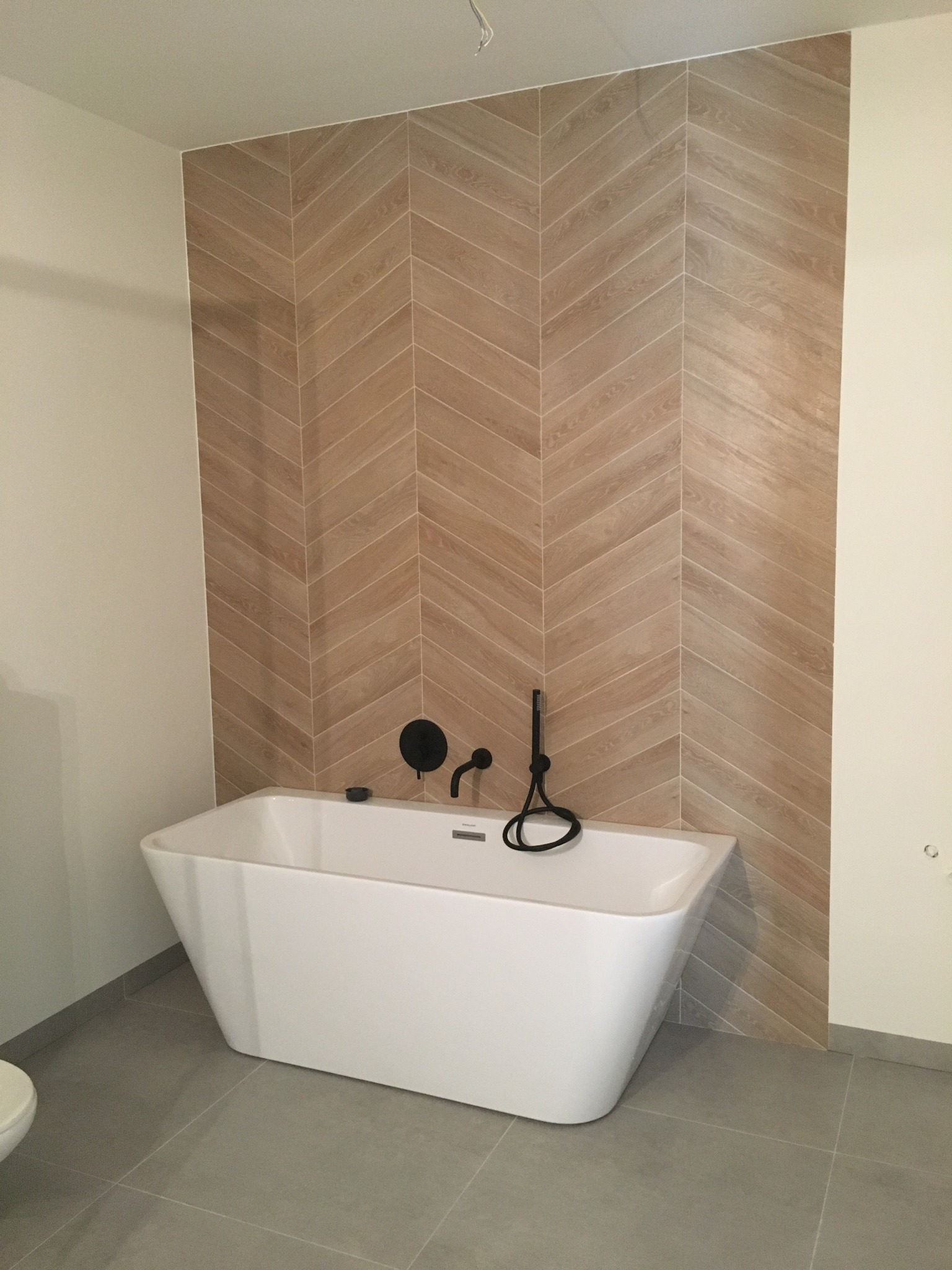 Nowoczesna łazienka z białą wanną wolnostojącą i ścianą wyłożoną płytkami w jodełkę, czarna bateria wannowa.