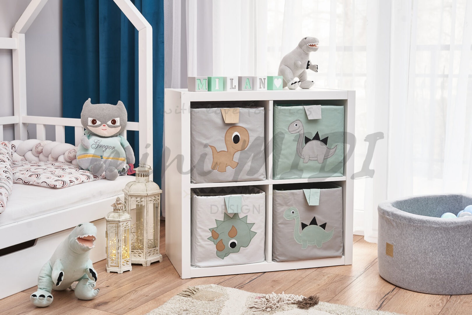 Pokój dziecięcy z białym łóżkiem w kształcie domku, regałem z materiałowymi pojemnikami z aplikacjami dinozaurów, pluszowymi zabawkami i suchym basenem z kulkami.
