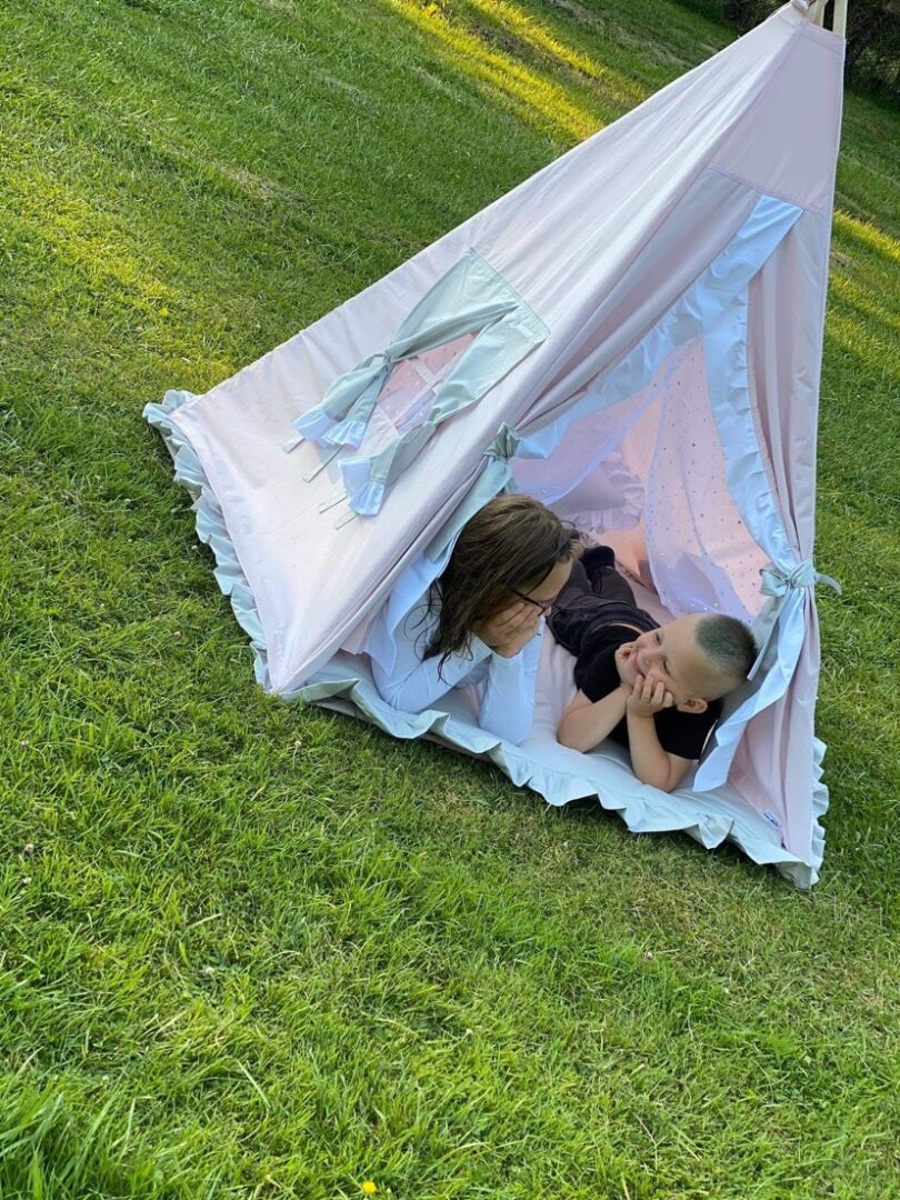 Dzieci bawią się w różowym tipi z falbankami na trawie w słoneczny dzień.