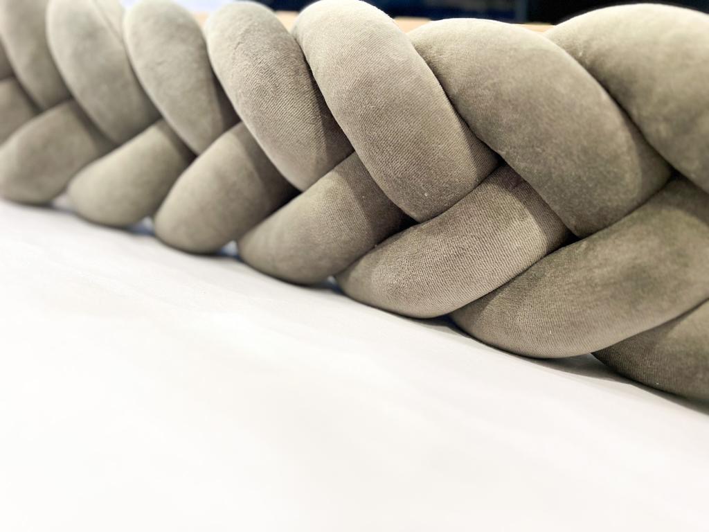 Beżowy warkocz ochronny do łóżeczka dziecięcego, wykonany z miękkiego materiału, leżący na białym tle.