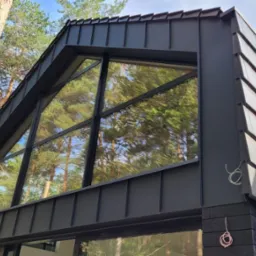 Nowoczesny dom z antracytowym dachem blaszanym i dużym oknem szczytowym, otoczony drzewami.