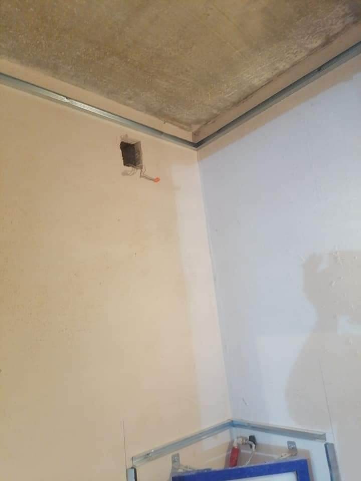 Wnętrze w trakcie remontu: surowy betonowy sufit z metalowymi profilami, ściana z otworem na instalację elektryczną i wystającymi przewodami.