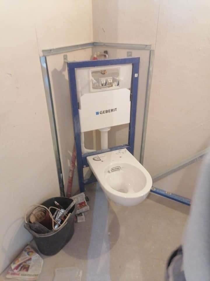 Wisząca toaleta marki Geberit zamontowana na metalowej ramie w trakcie remontu łazienki, widoczny kubeł z narzędziami i resztki materiałów budowlanych.