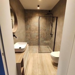 REMHOME - Nowoczesna łazienka z kabiną prysznicową typu walk-in z czarną ramą, umywalką nablatową na szafce z drewnianym blatem, okrągłym lustrem i płytkami w odcieniach beżu i brązu.