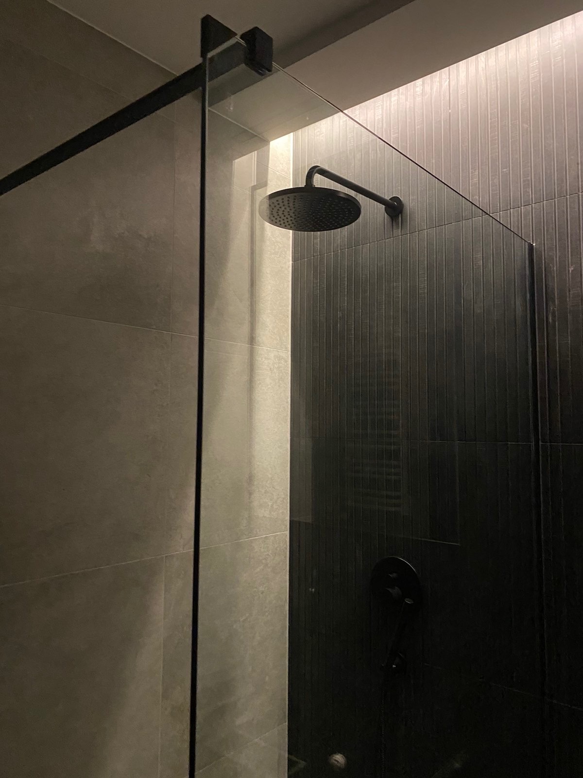 Nowoczesna kabina prysznicowa z czarną armaturą, szklana ściana z minimalistycznym uchwytem, płytki w odcieniach szarości z subtelną fakturą.