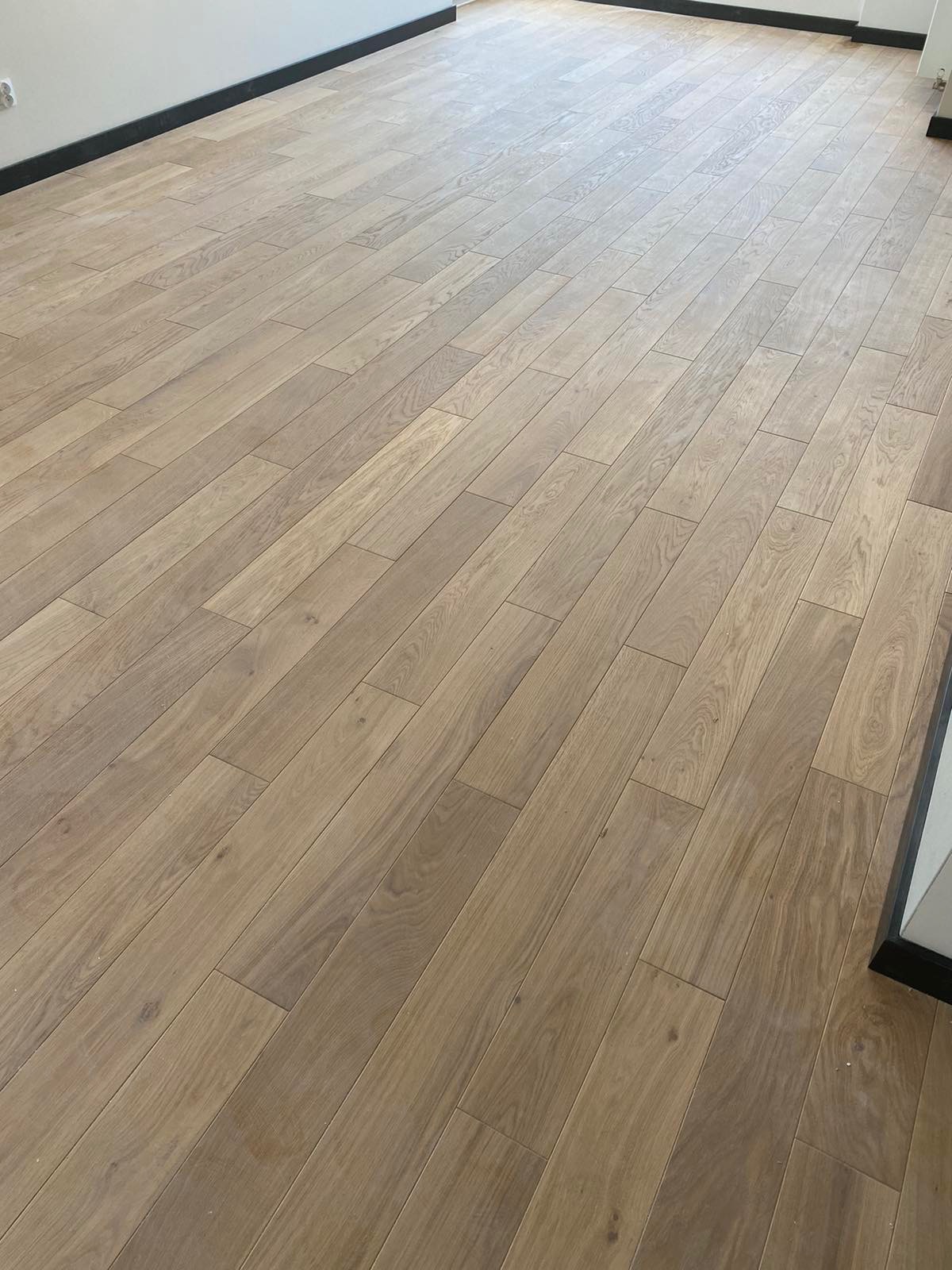 Ułożona podłoga z jasnych paneli drewnopodobnych z widoczną strukturą drewna, czarna listwa przypodłogowa.