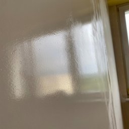 Mateusz Warot - Błyszcząca, gładka ściana po malowaniu, z widocznym odbiciem okna. Jasny odcień farby, delikatne refleksy światła podkreślają równą powierzchnię.