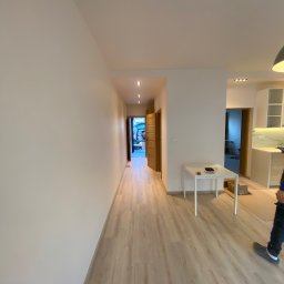 Usługi Ogólnobudowlane Zoch-Bud - Jasne panele podłogowe w przedpokoju po remoncie, białe ściany, widoczne drzwi i fragment kuchni. Neutralne oświetlenie, minimalistyczny wystrój.