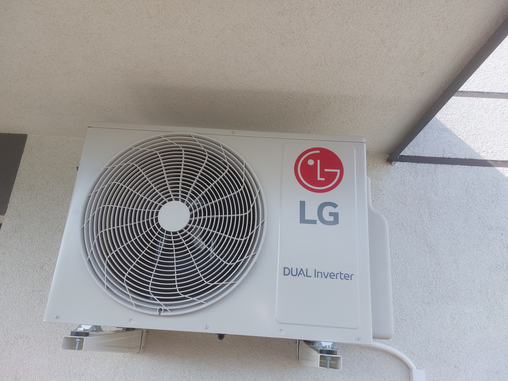 Zewnętrzna jednostka klimatyzatora LG Dual Inverter zamontowana na elewacji budynku, widoczna z dołu pod kątem, z fragmentem dachu w tle.