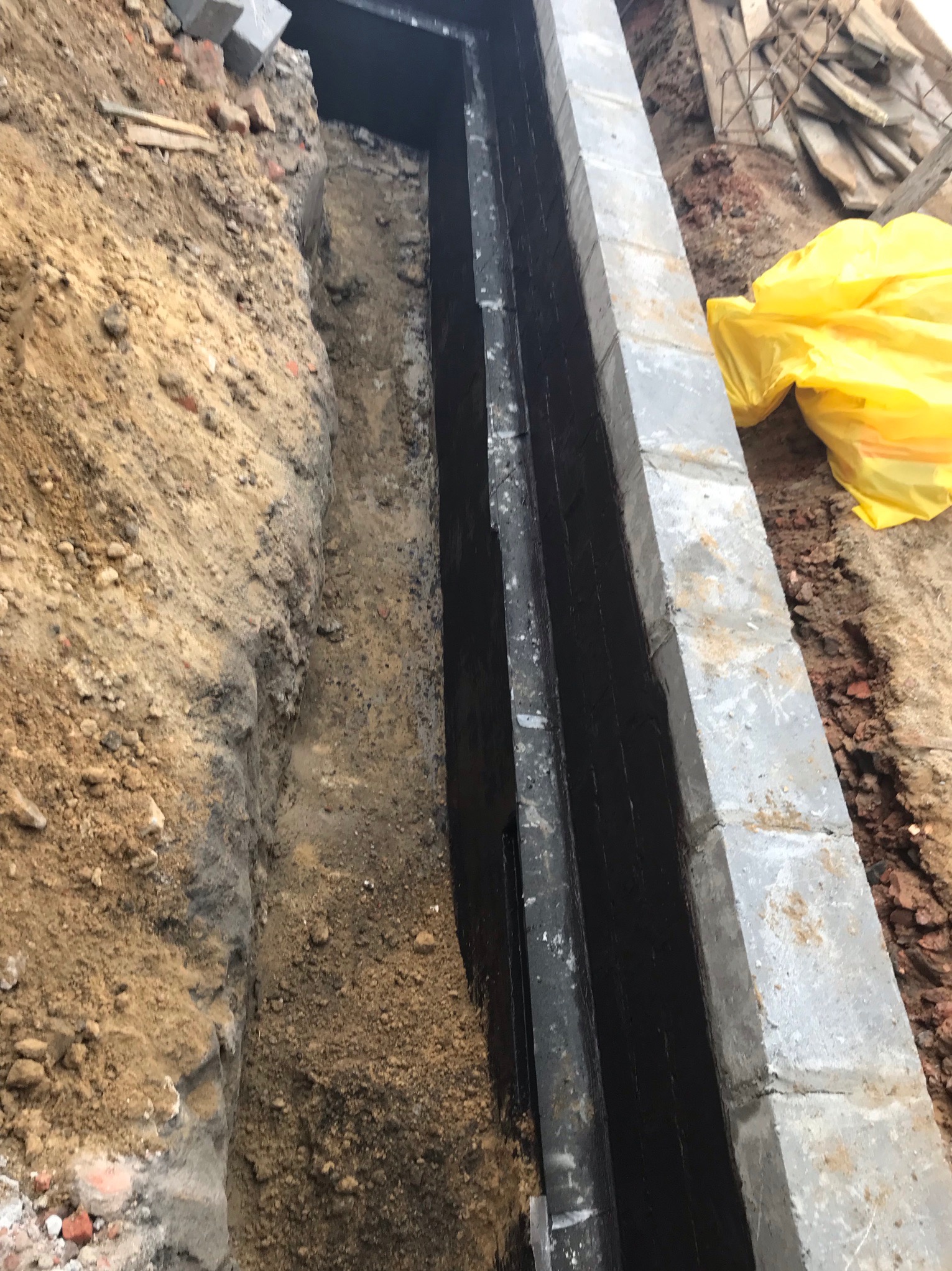 Wykop pod fundament z izolacją przeciwwilgociową, widoczne cegły i żółta folia zabezpieczająca