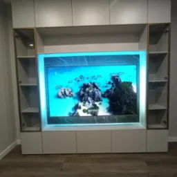 Biała zabudowa meblowa z podświetleniem LED wokół wnęki na telewizor, z przeszklonymi szafkami po bokach, na drewnianej podłodze.