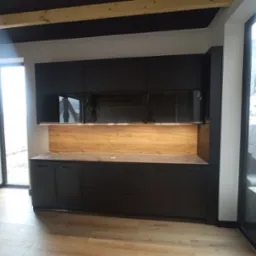 Nowoczesna, czarna zabudowa kuchenna z drewnianym panelem dekoracyjnym, oświetleniem LED i odbiciem okna w szklanych frontach szafek wiszących.