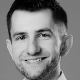 Portret uśmiechniętego mężczyzny z krótką brodą, w czerni i bieli, z wyraźnie zaznaczonymi zmarszczkami mimicznymi wokół oczu.