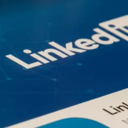 Ekran urządzenia z logo LinkedIn na niebieskim tle z geometrycznym wzorem, widoczny fragment profilu LinkedIn.