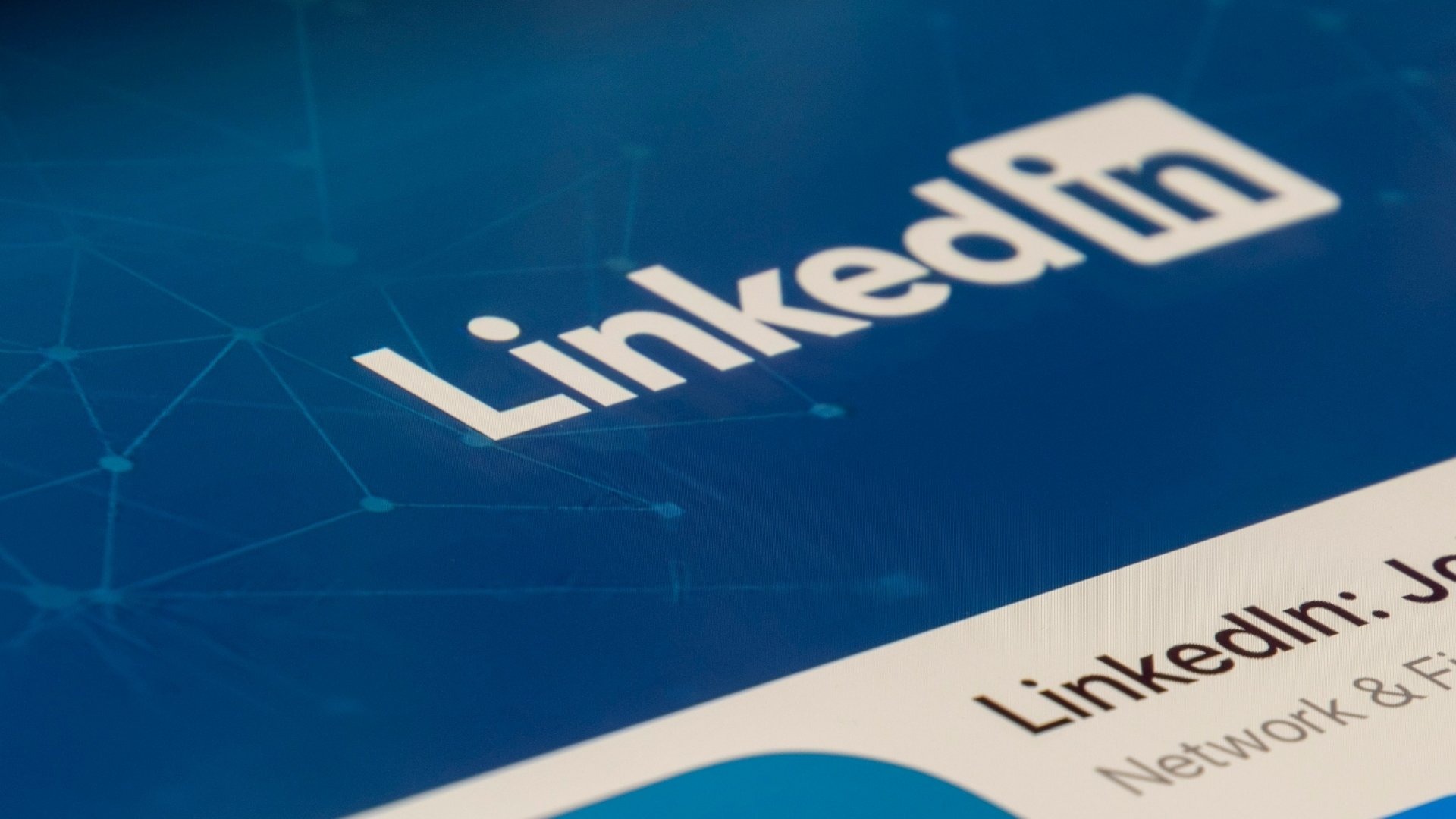 Ekran urządzenia z logo LinkedIn na niebieskim tle z geometrycznym wzorem, widoczny fragment profilu LinkedIn.
