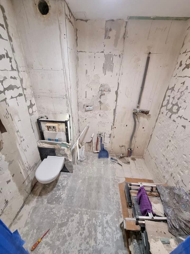 Wnętrze łazienki w trakcie remontu, widoczne przygotowane ściany, zamontowana toaleta, narzędzia i materiały budowlane.