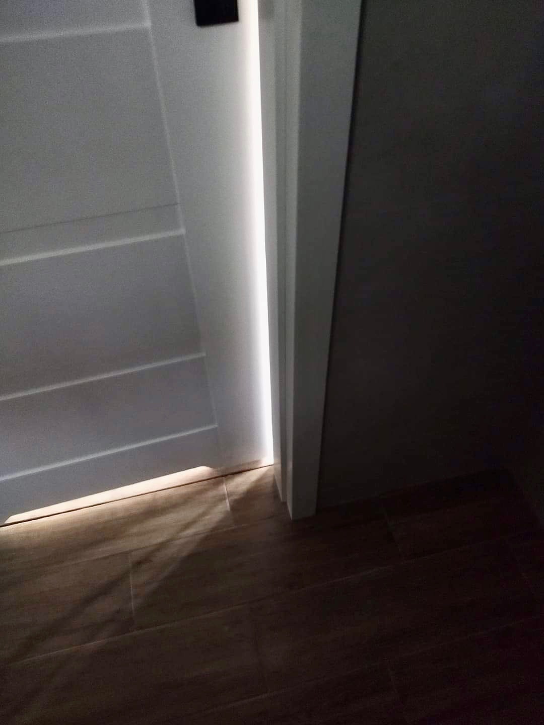 Szczelina w drzwiach wewnętrznych, przez którą wpada światło, oświetlając drewnopodobną podłogę.