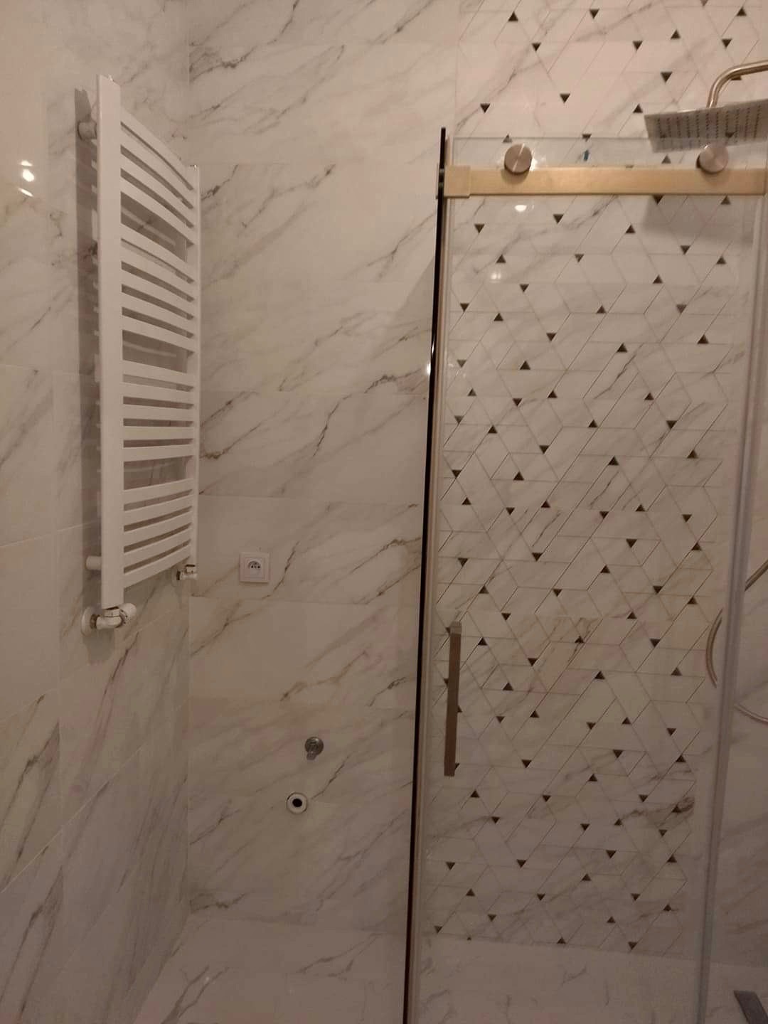 Nowoczesna łazienka z marmurowymi płytkami, grzejnikiem drabinkowym i kabiną prysznicową z geometrycznym wzorem na szkle.