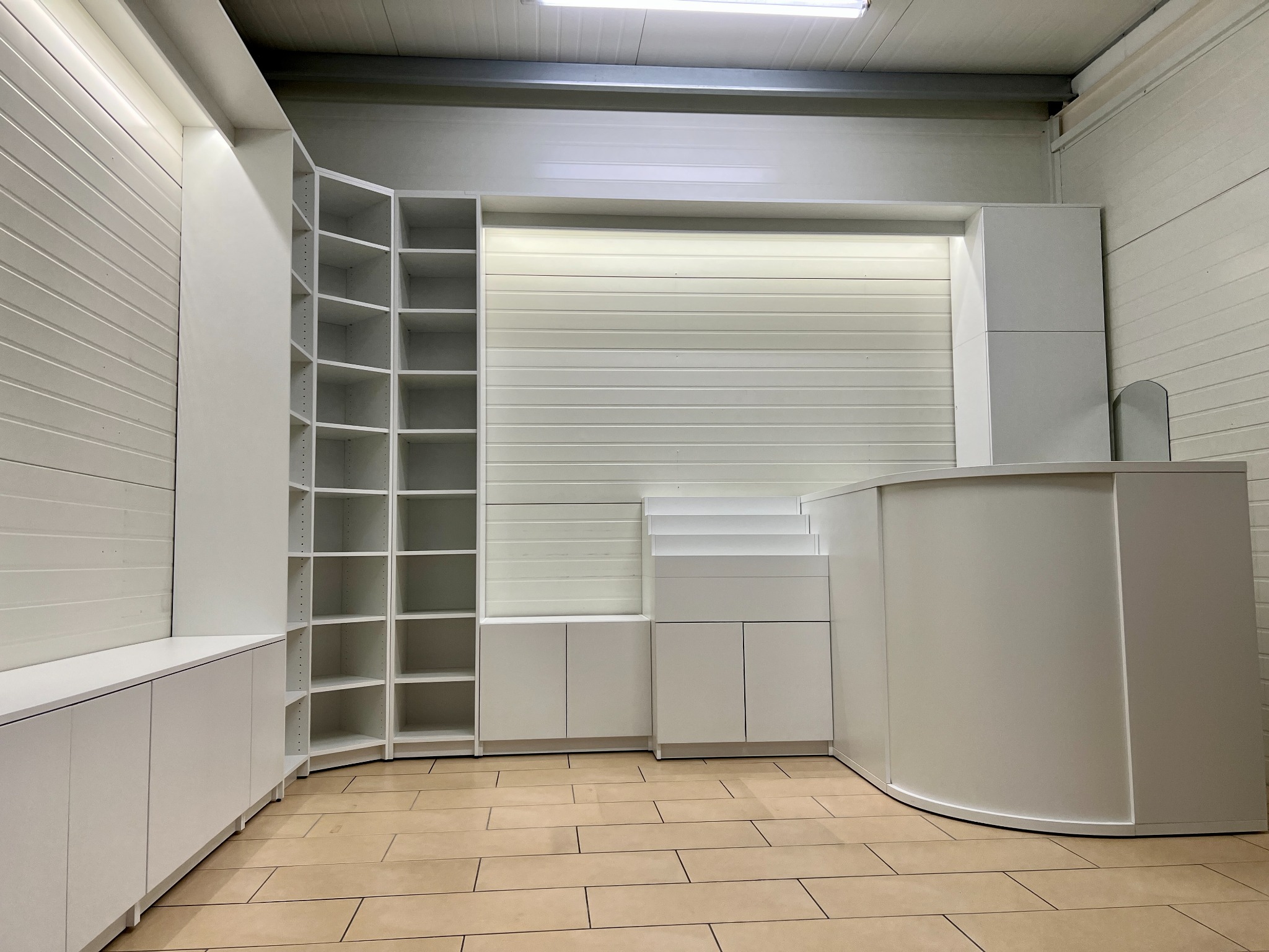 Białe, modułowe meble z półkami i szafkami, wykonane na wymiar, ustawione w przestronnym pomieszczeniu z jasną podłogą i oświetleniem sufitowym.