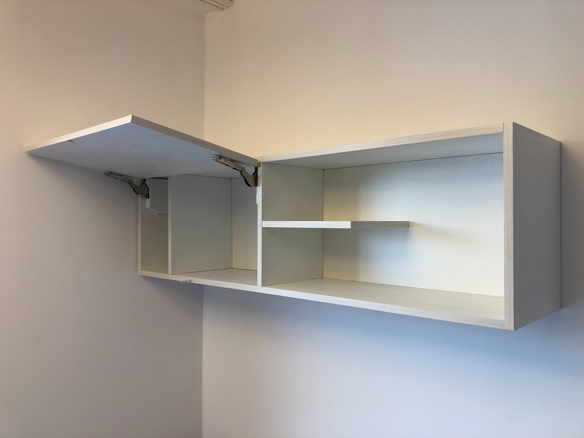 Półka wisząca z białego drewna z otwartymi drzwiczkami, widoczne metalowe zawiasy i wewnętrzna półka, minimalistyczny design.