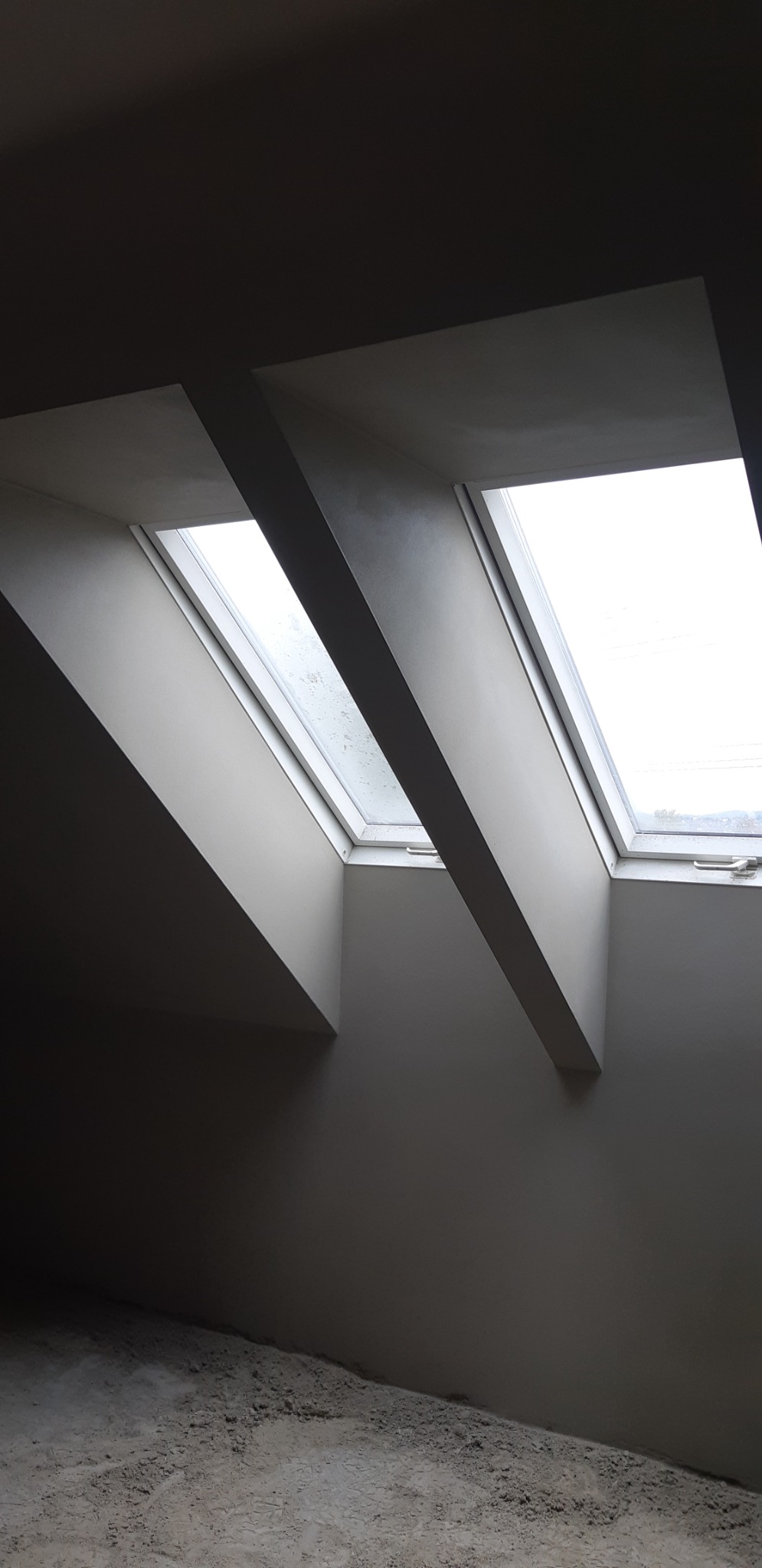 Świeżo otynkowane poddasze z dwoma oknami dachowymi, widoczne ślady po pracach na podłodze.