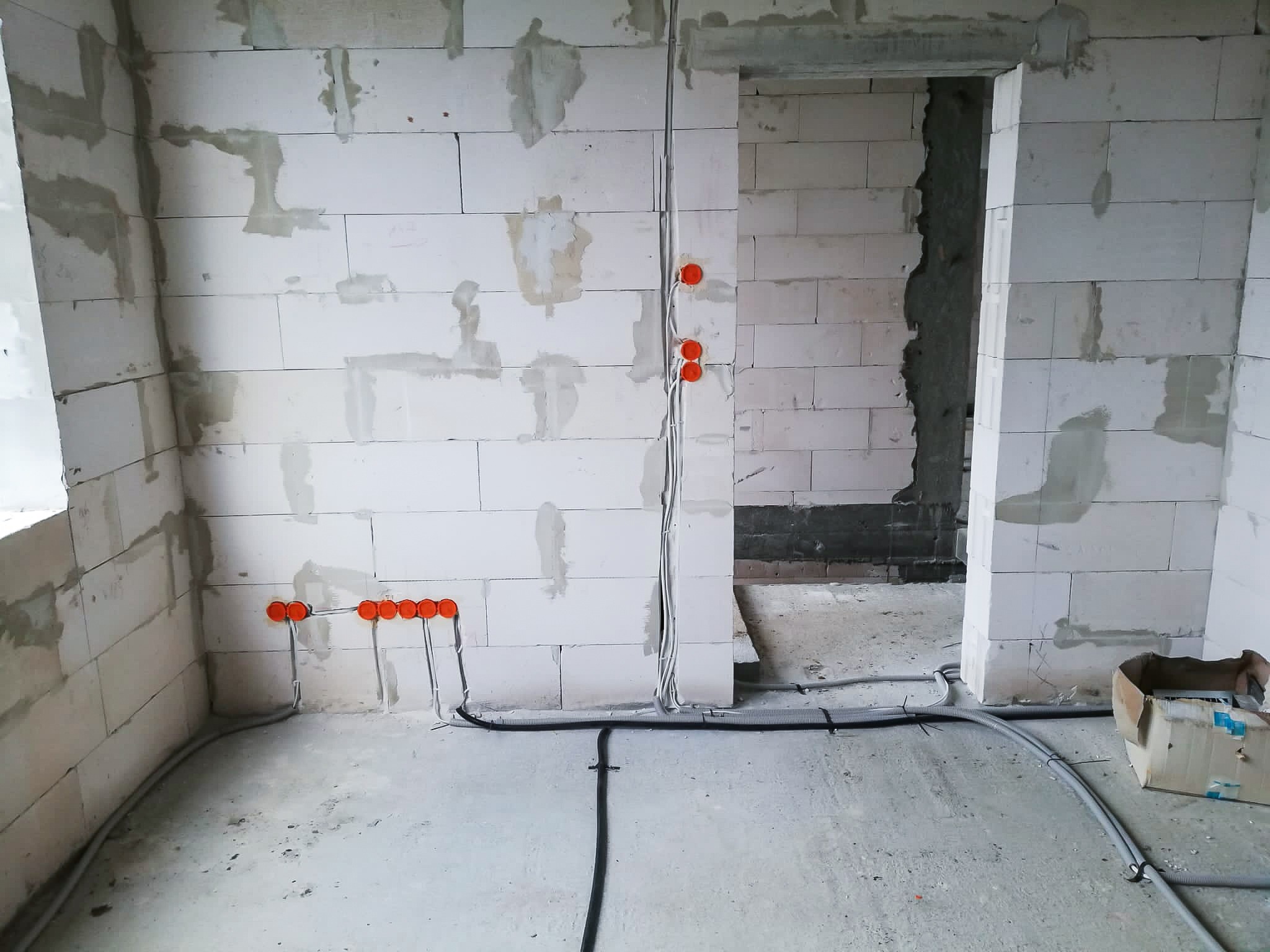 Surowy stan: instalacja elektryczna w trakcie montażu w pomieszczeniu z białych bloczków, widoczne przewody w peszlach i pomarańczowe puszki pod gniazdka.