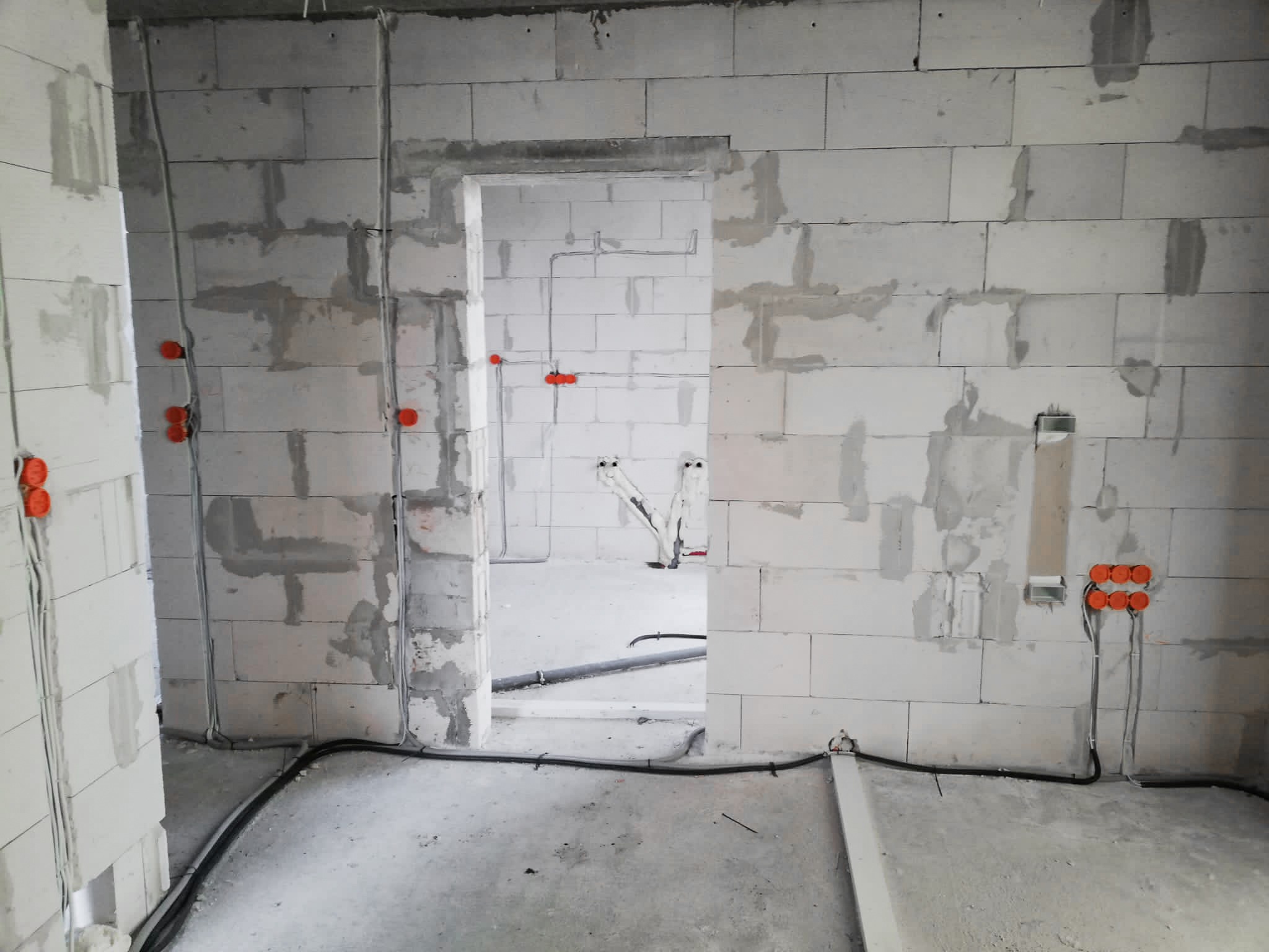 Surowy stan instalacji elektrycznej w nowym budynku z widocznymi przewodami, puszkami instalacyjnymi i fragmentami ścian z betonu komórkowego.