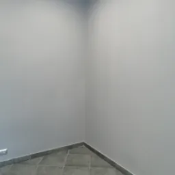 Pomalowane na szaro wnętrze pokoju z szarą podłogą z płytek i listwami przypodłogowymi. Widoczne gniazdko elektryczne po lewej stronie.