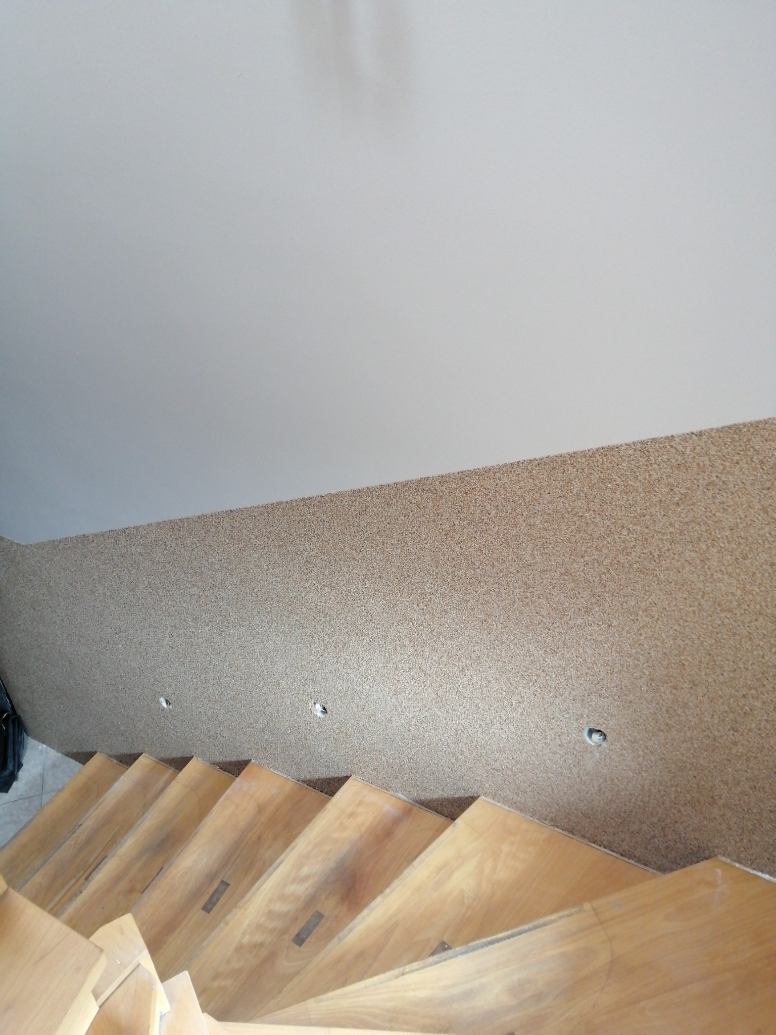 Widok z góry na drewniane schody z teksturalną, beżową ścianą i wpuszczonymi punktami świetlnymi w tle.