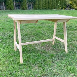Wiktor Lewandowicz Wooden Solutions - Surowy, jasny, drewniany stół z dwiema szufladami, stojący na trawie w ogrodzie, widoczne niedoskonałości obróbki drewna na nogach
