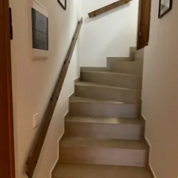 Wewnętrzne schody z brązowymi stopniami i drewnianą poręczą zamontowaną po lewej stronie, widok z dołu do góry.