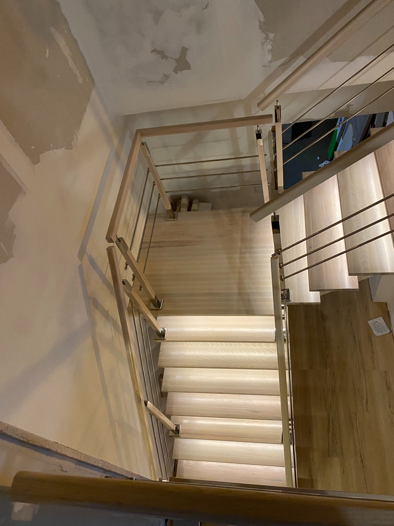 Jasne drewniane schody z metalową balustradą, widok z góry, ściany w trakcie wykończenia. Nowoczesny design z oświetleniem stopni.