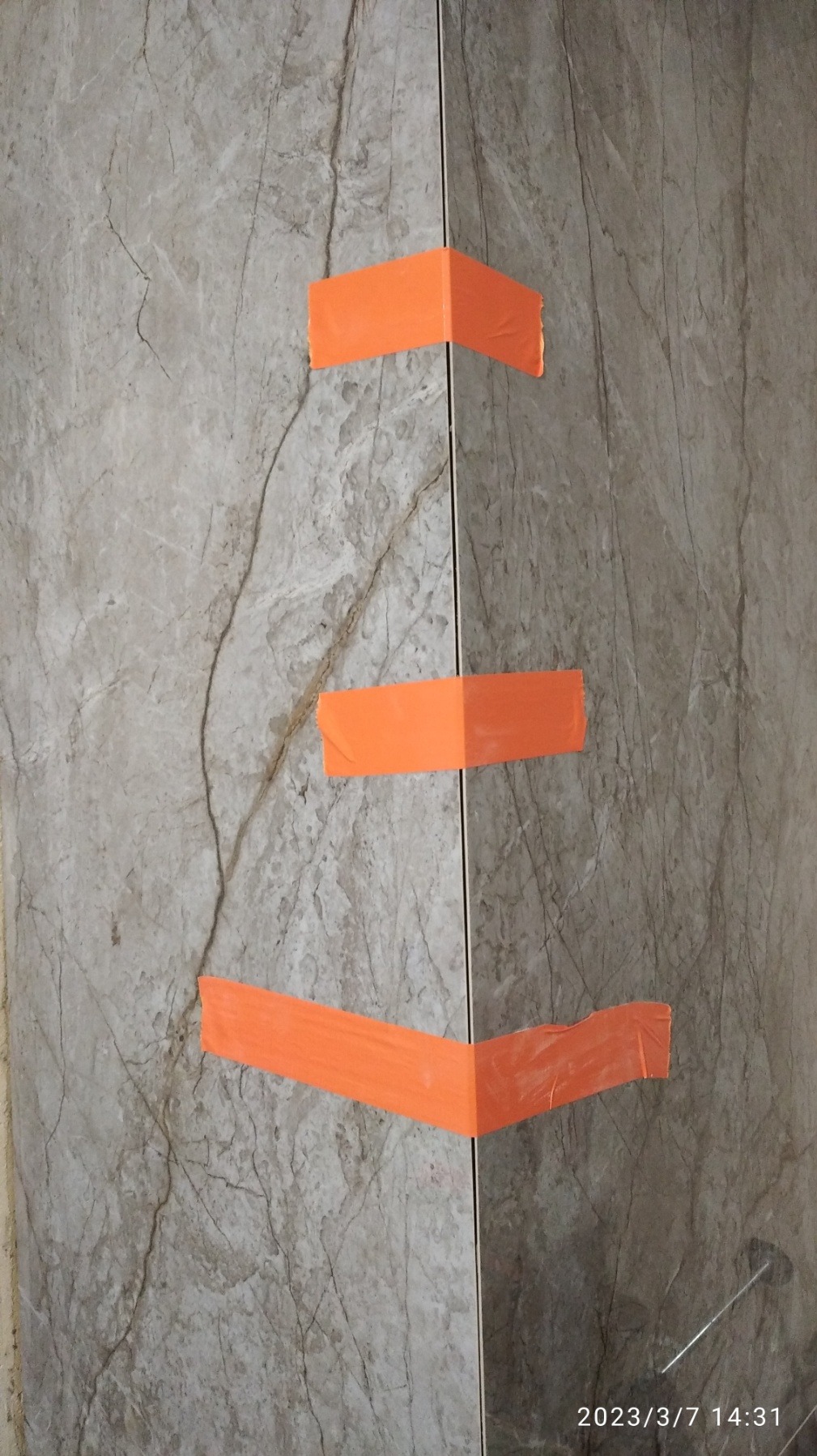 Ułożone płytki imitujące marmur, zabezpieczone pomarańczową taśmą malarską na rogach i krawędziach, widoczny etap prac glazurniczych.