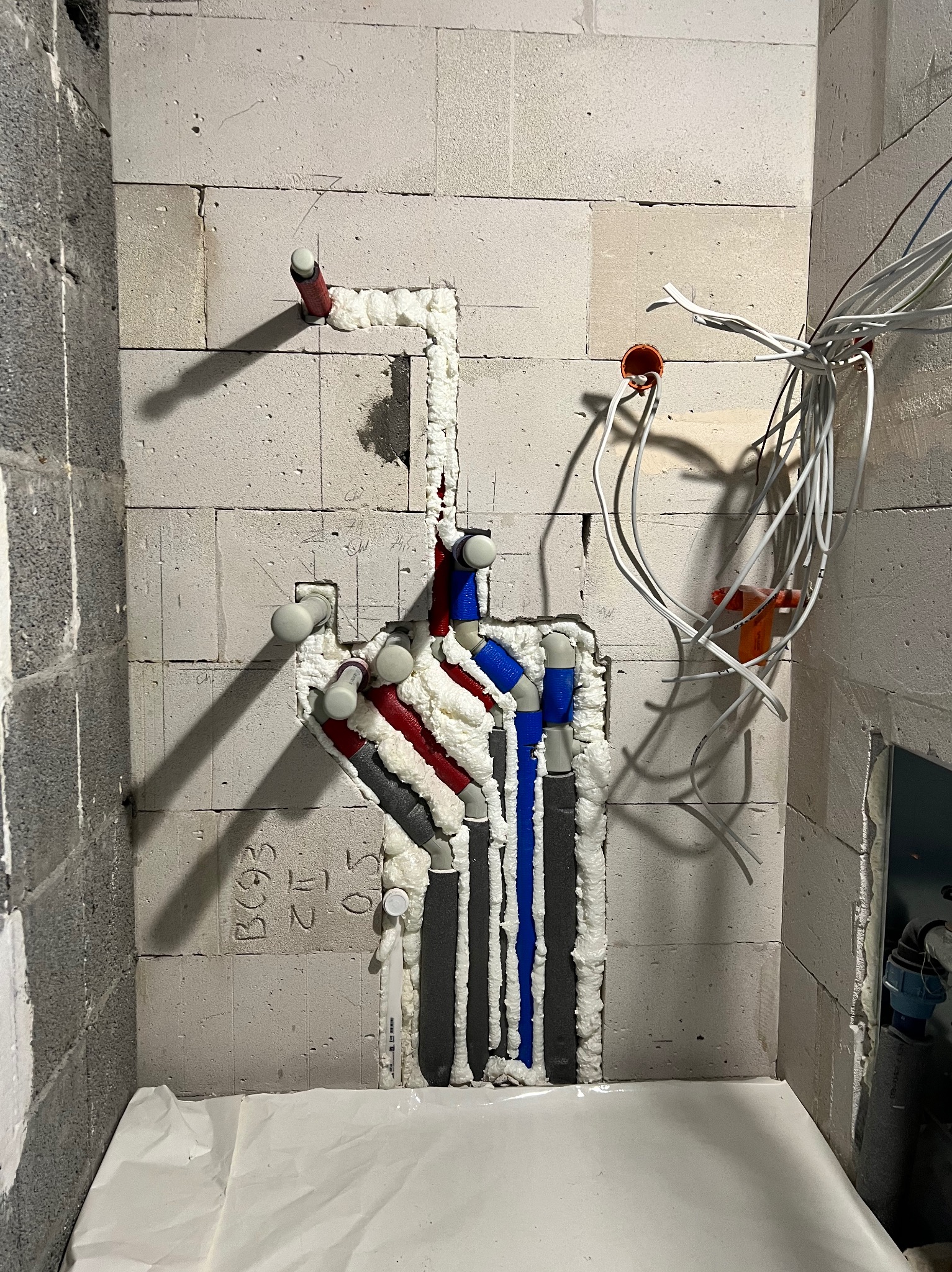Instalacja wodna i elektryczna w trakcie montażu w surowym wnętrzu, rury w izolacji piankowej, przewody zwisające ze ściany, zabezpieczona podłoga.