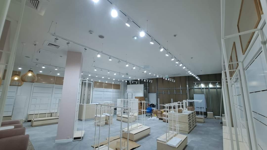 Wnętrze sklepu w trakcie instalacji oświetlenia szynowego, widoczne także elementy wyposażenia i kartony.