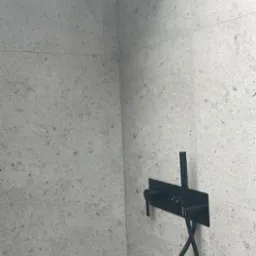 Nowoczesna kabina prysznicowa z czarną armaturą na tle szarych, kamiennych płytek.