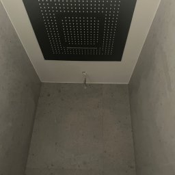 Usługi leśne - Nowoczesna kabina prysznicowa z kwadratową, czarną deszczownicą sufitową i szarymi płytkami imitującymi kamień, widoczne wystające przewody.