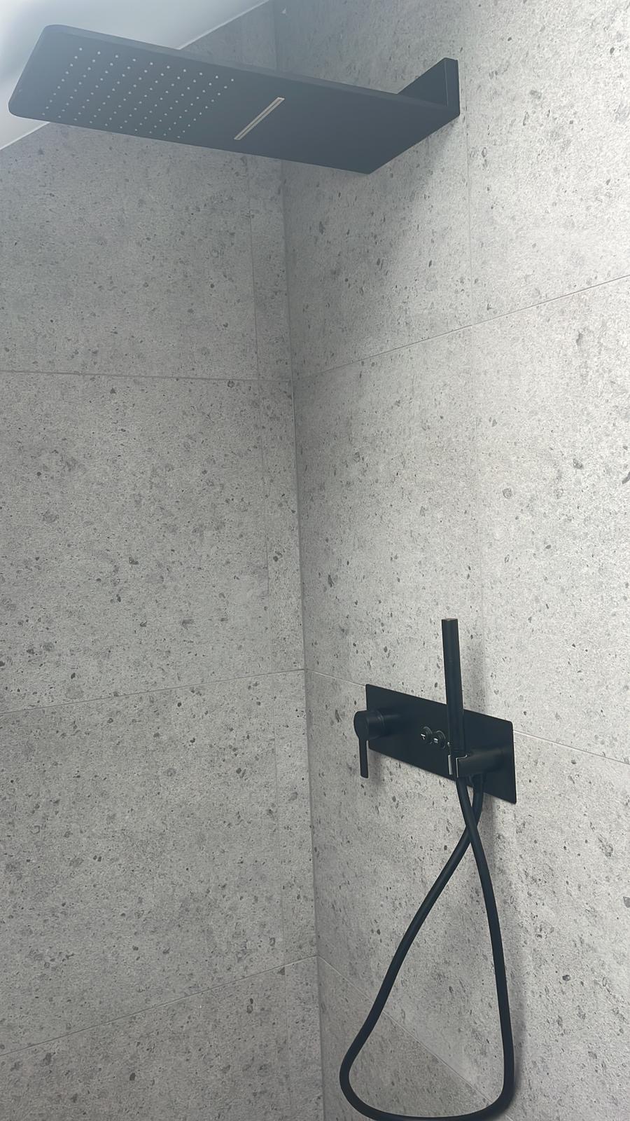 Nowoczesna kabina prysznicowa z czarną armaturą na tle szarych, kamiennych płytek.