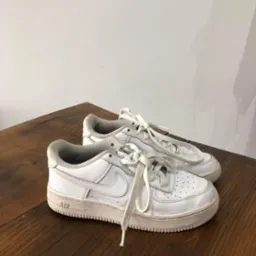 Para białych, lekko zabrudzonych butów sportowych Nike Air Force 1 na drewnianym stole, sznurówki rozwiązane.
