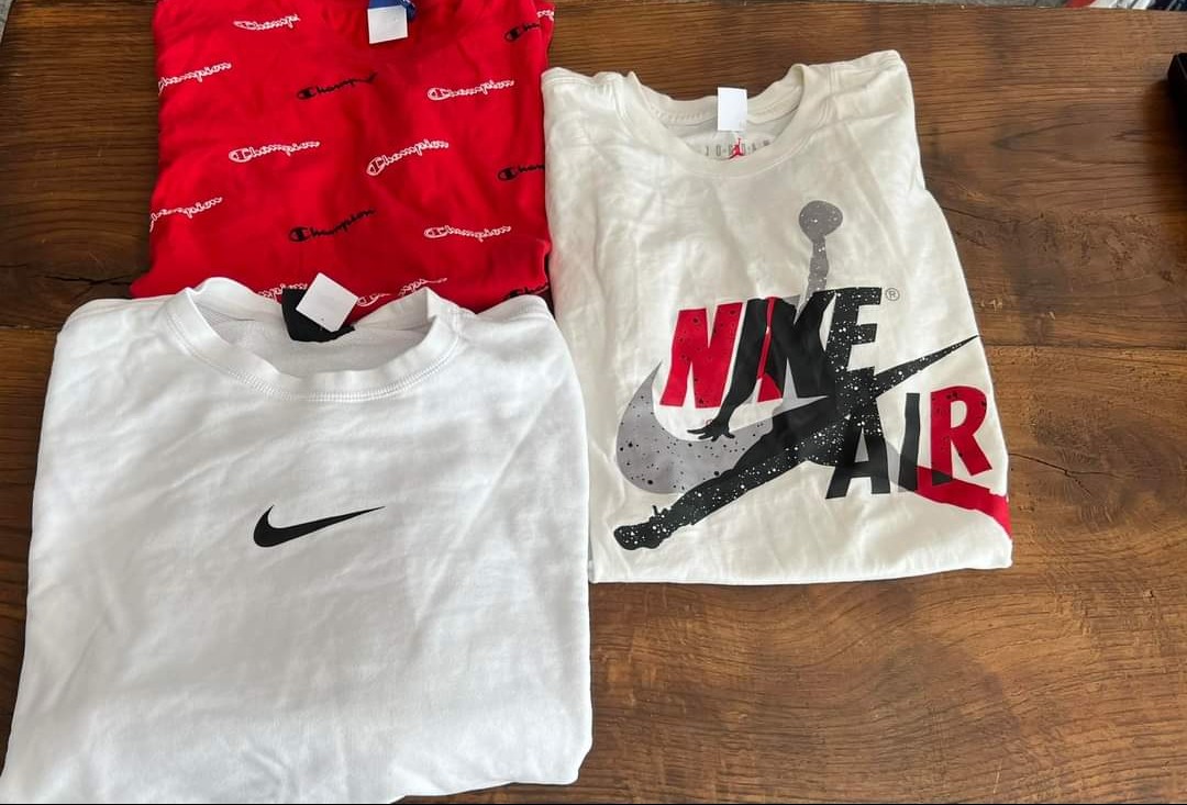 Zestaw trzech poskładanych koszulek: czerwonej z logo Champion, białej z logo Nike i kremowej z grafiką Nike Air Jordan, prezentowany przez firmę odzieżową z Kraśnika.