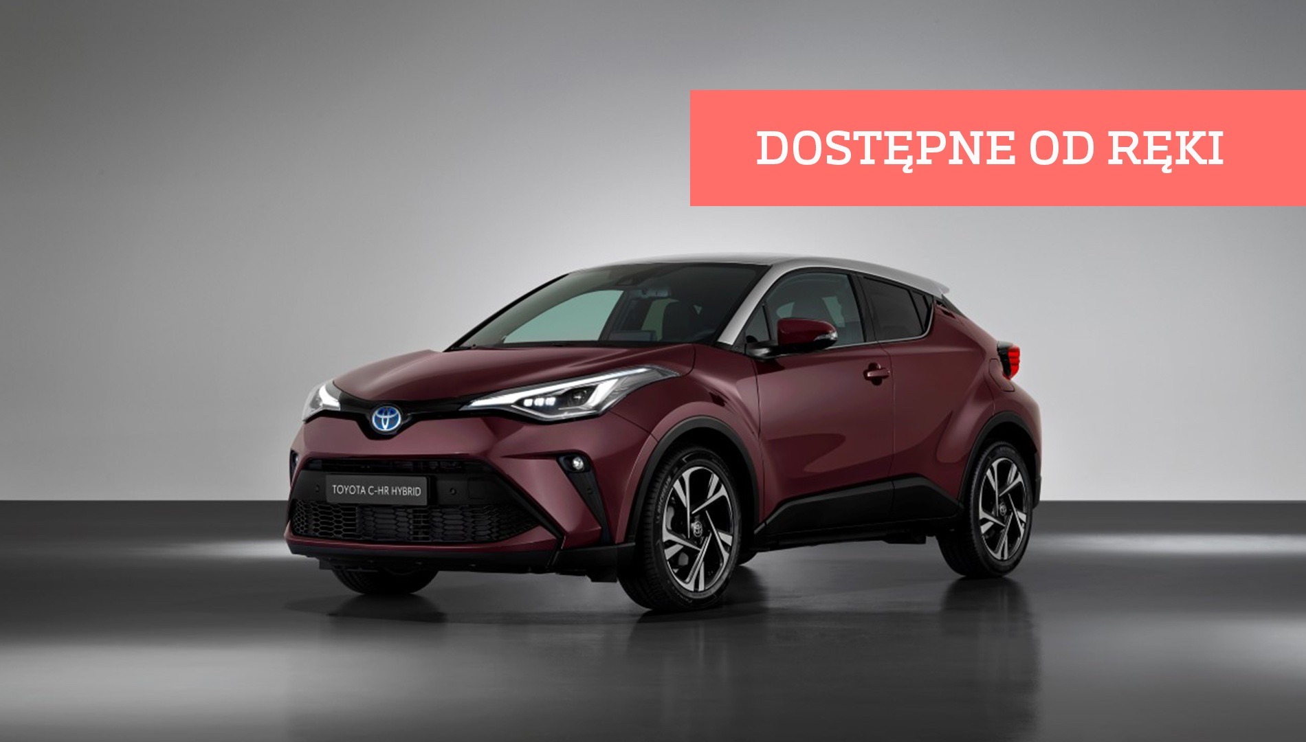 Bordowy hybrydowy crossover Toyota C-HR z srebrnym dachem, prezentowany na szarym tle z napisem 'Dostępne od ręki'.
