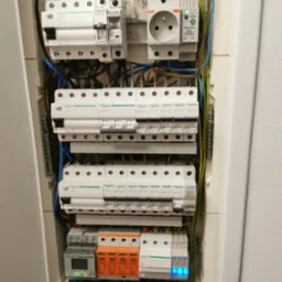 Otwarta skrzynka elektryczna z zainstalowanymi bezpiecznikami Schneider Electric, wyłącznikami różnicowoprądowymi, licznikiem 3-fazowym Qubino i zabezpieczeniem przeciwprzepięciowym Vcx, widoczne...