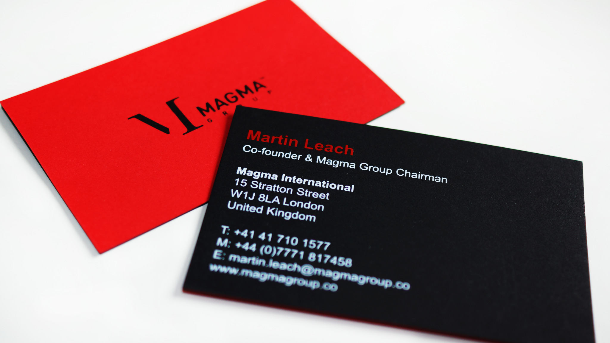 Dwie wizytówki: jedna czerwona z czarnym logo, druga czarna z białym tekstem informacyjnym o firmie i jej pracowniku na białym tle.