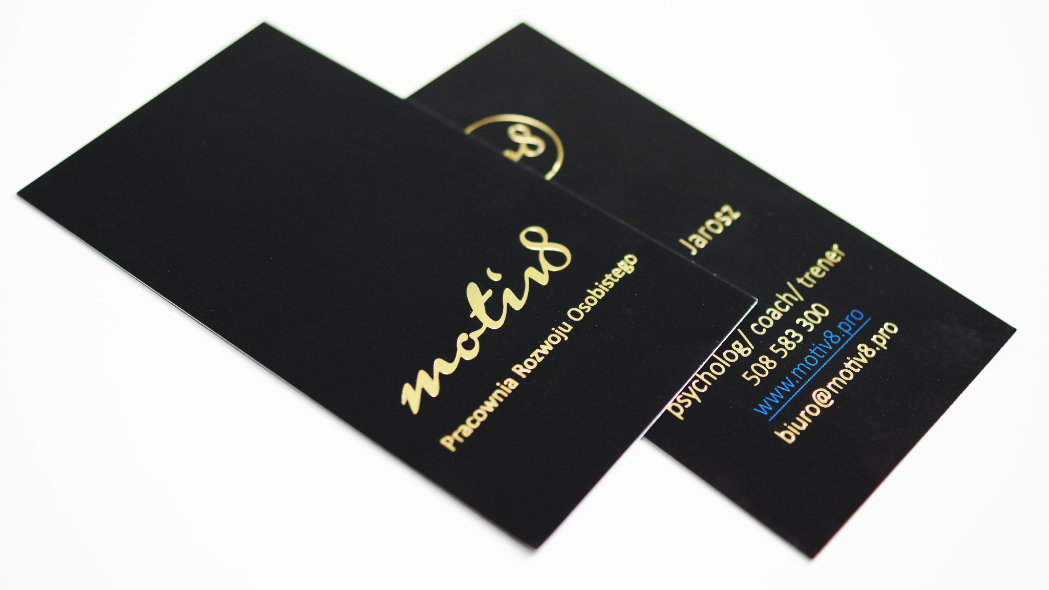Dwie czarne wizytówki z błyszczącym, złotym nadrukiem: logo, nazwa firmy 'motiv8 Pracownia Rozwoju Osobistego' oraz dane kontaktowe psychologa, trenera Jarosza.