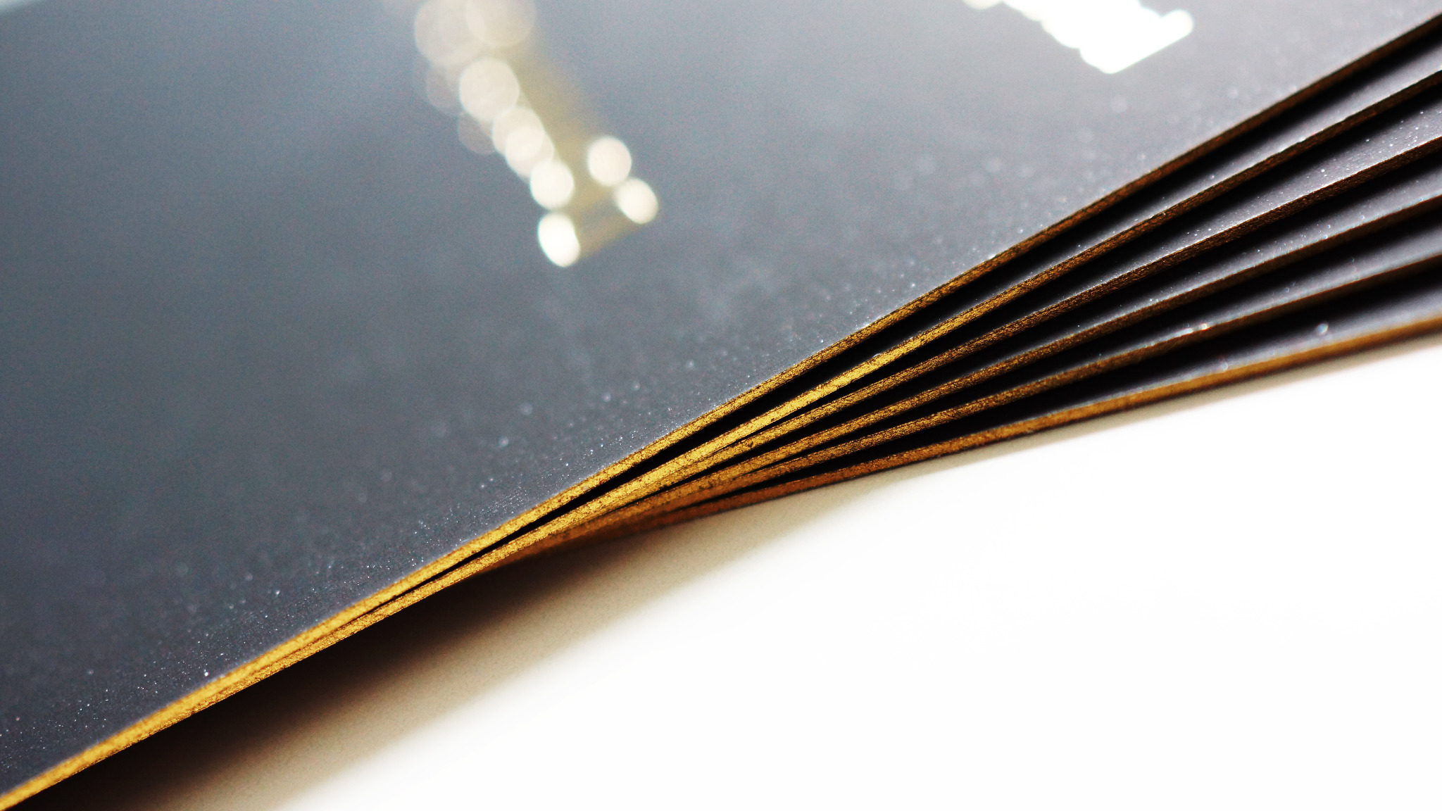 Stos wizytówek z czarnym tłem i złotymi brzegami, ułożonych pod kątem, z widoczną fakturą papieru.