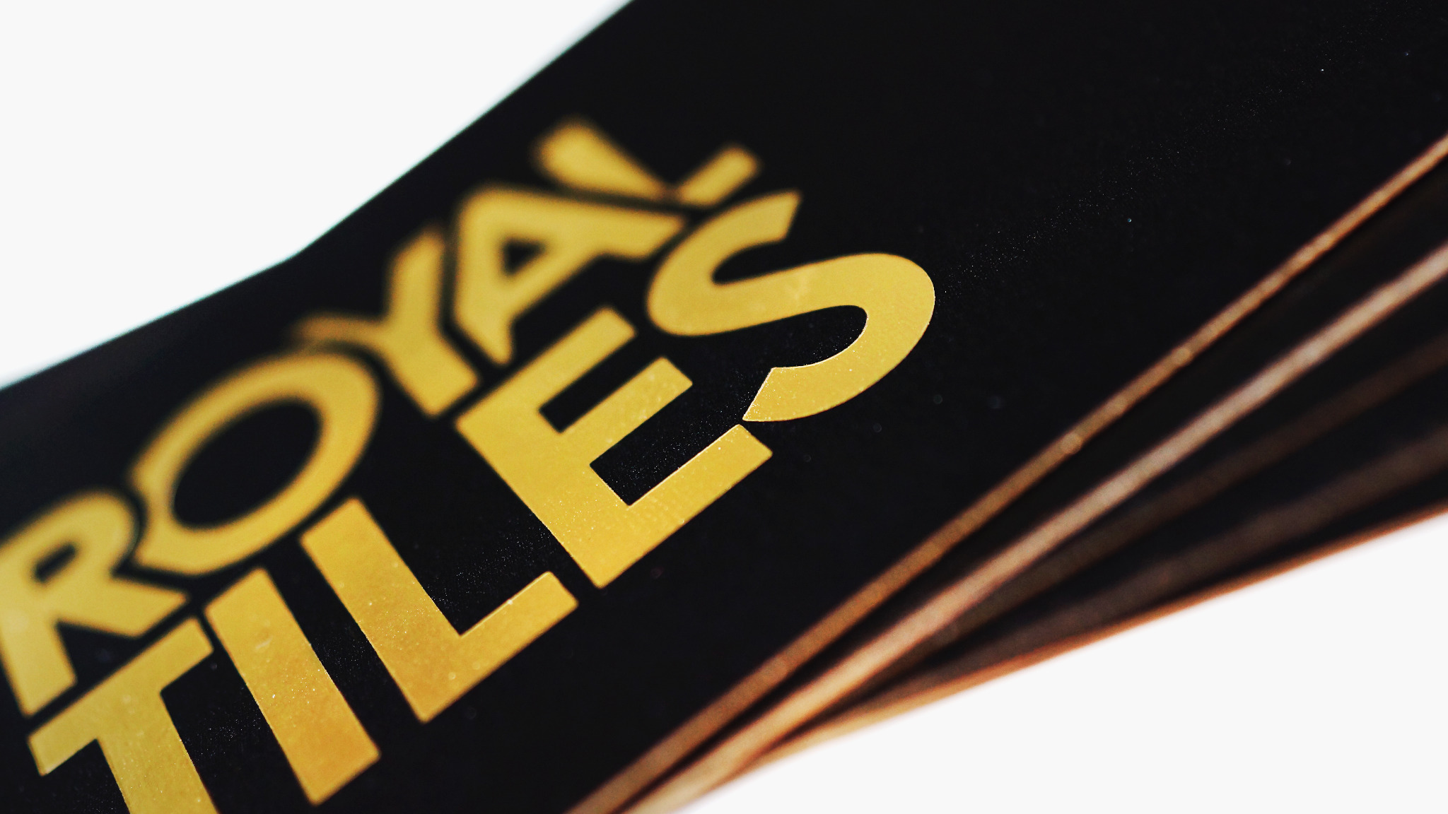 Stos czarnych wizytówek z błyszczącym, złotym napisem 'ROYAL TILES', ułożonych pod kątem na białym tle.